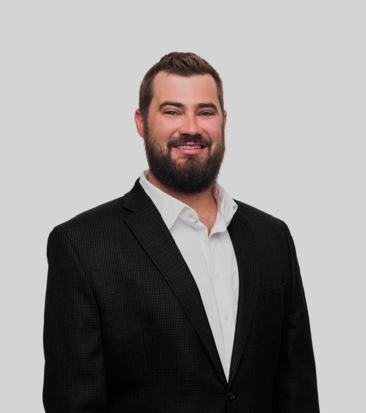 A man with a beard is wearing a black suit and white shirt.