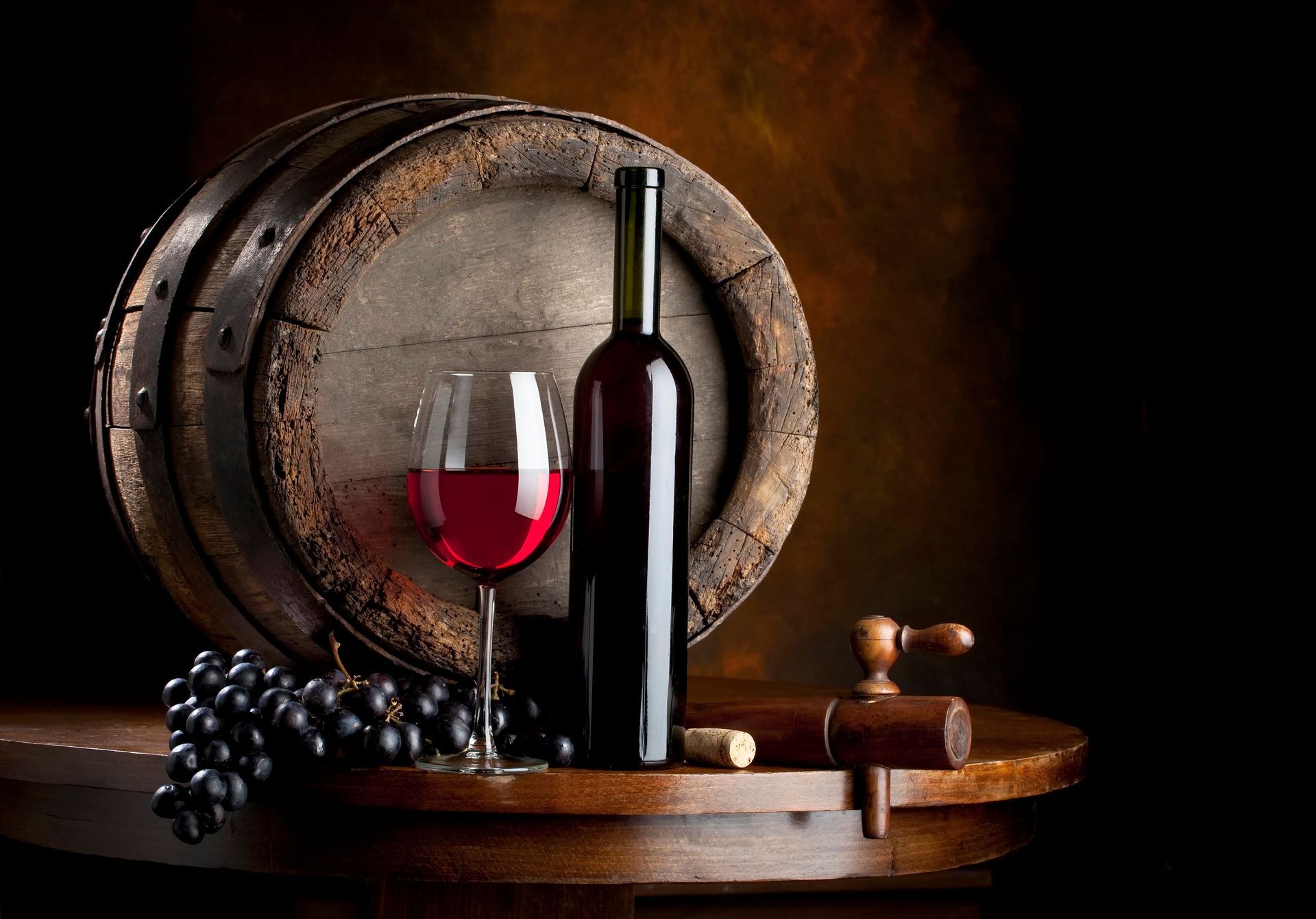 Bottiglia di vino, bicchiere pieno, uva e botte su un tavolo di legno, sfondo scuro.