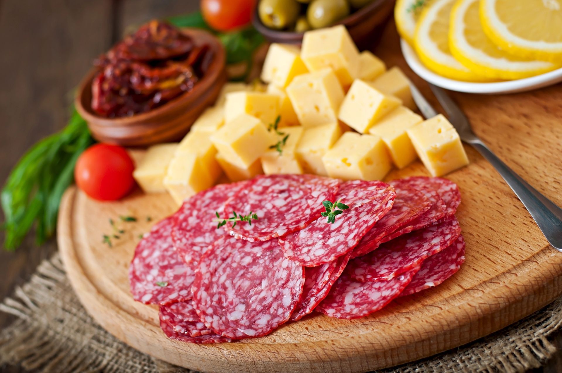 Fette di salame con formaggio a cubetti, pomodori secchi, olive, fette di limone e pomodori su un tagliere di legno.