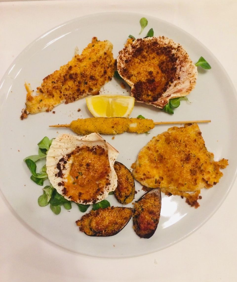 Piatto di frutti di mare impanati, tra cui capesante, cozze e uno spiedino, guarnito con verdure e limone.
