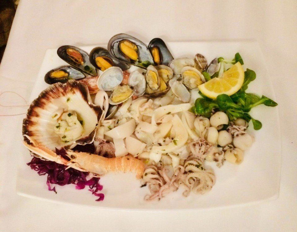 Piatto di frutti di mare con cozze, vongole, capesante, polpo e limone su un piatto bianco.