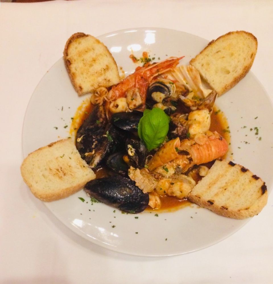 Stufato di pesce con cozze, gamberi e pane tostato su un piatto bianco.