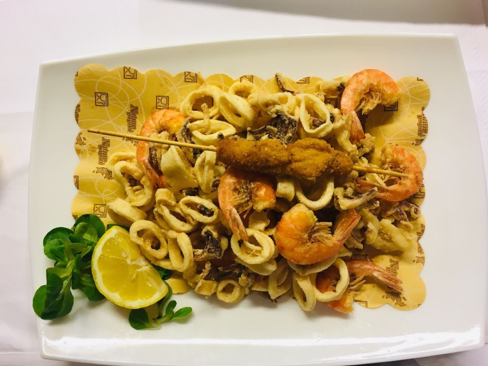 Piatto di pesce fritto con gamberi, calamari e spicchio di limone su un piatto decorativo.