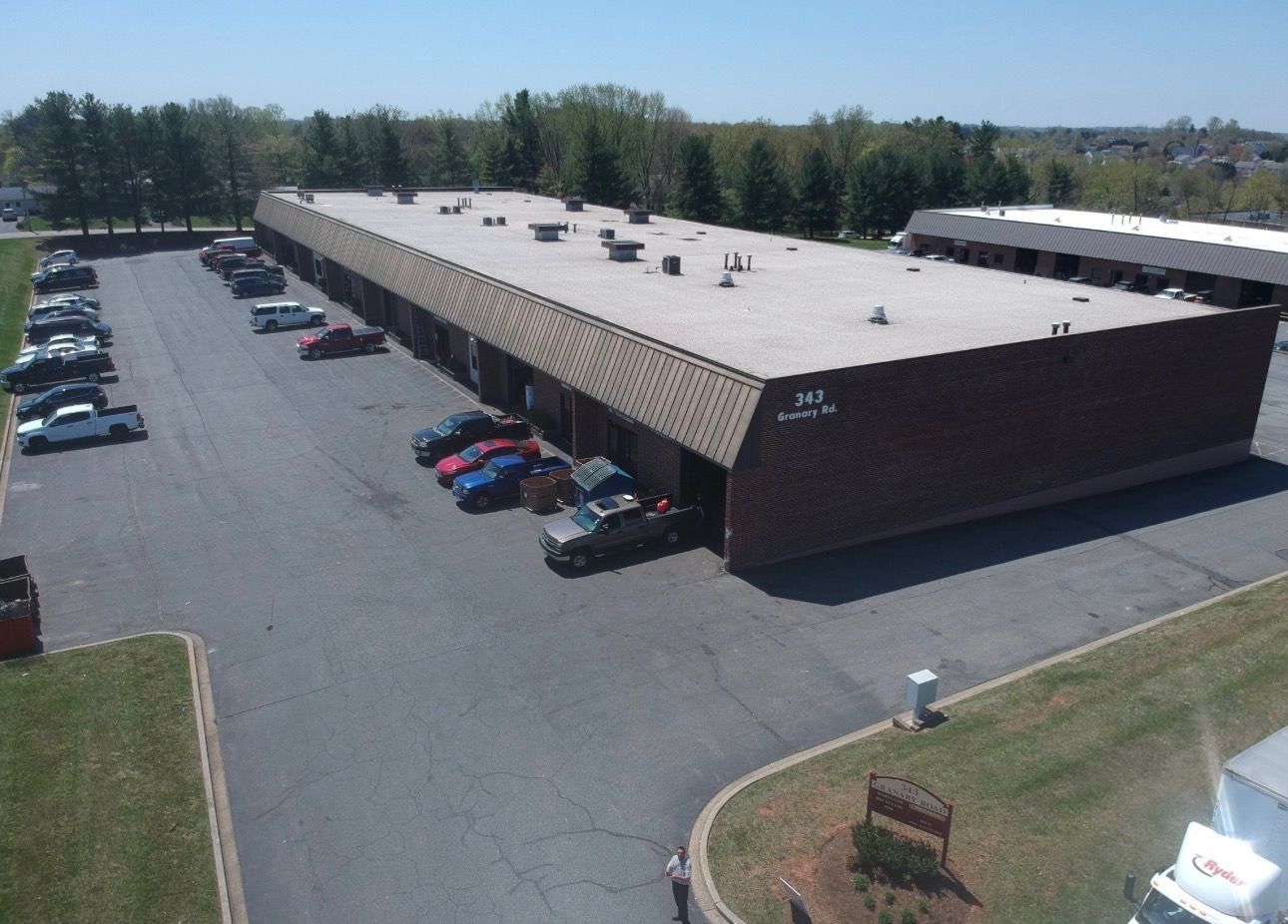 An aerial view of a single-story brick commercial building with a parking lot containing several cars on a sunny day.