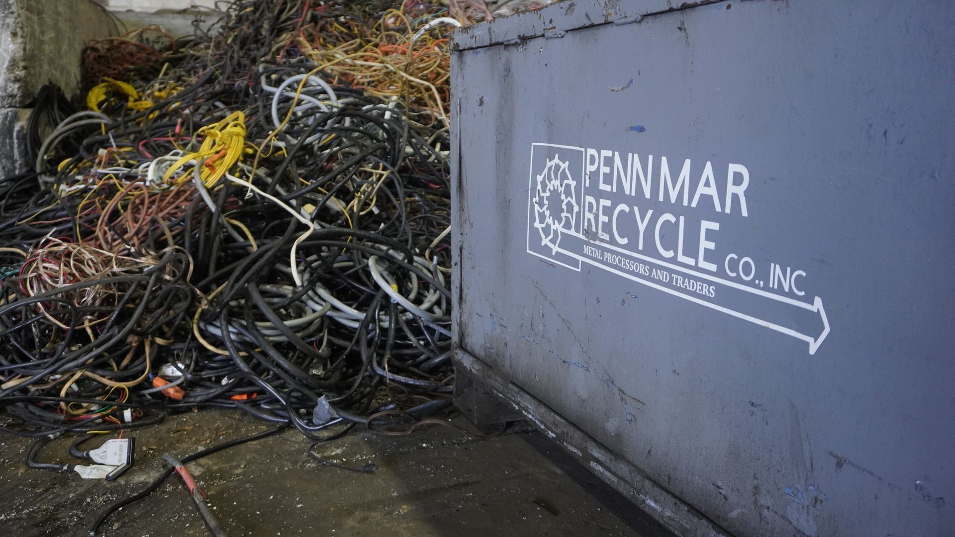 Overflowing pile of scrap metal beside a gray Pennmar Recycle container.
