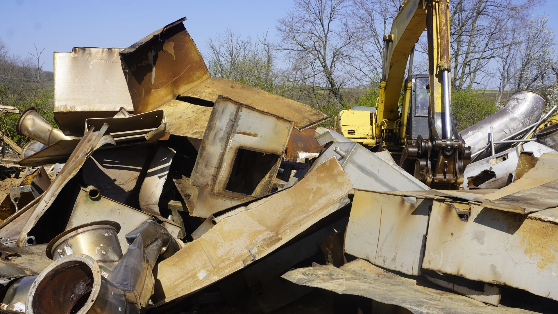 Bulldozer amid a pile of scrap metal and wrecked appliances in an outdoor junkyard.