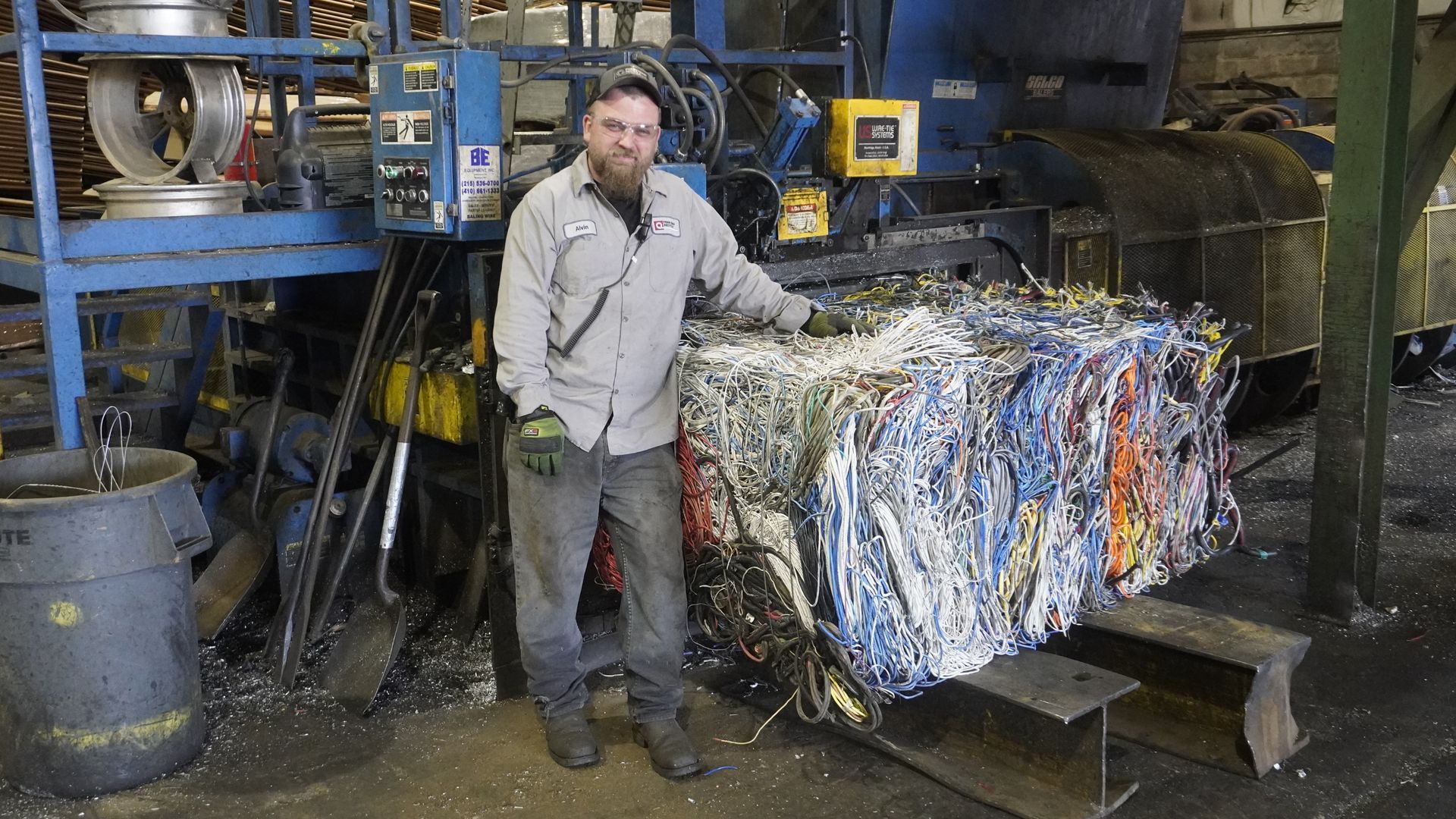 Worker stands beside a large bale of shredded recycling in an industrial facility.