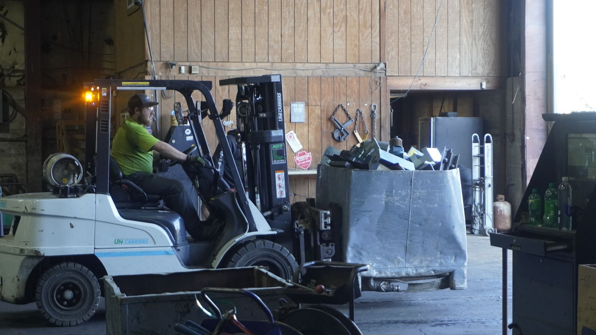Forklift operator moving a large metal bin inside an industrial warehouse.