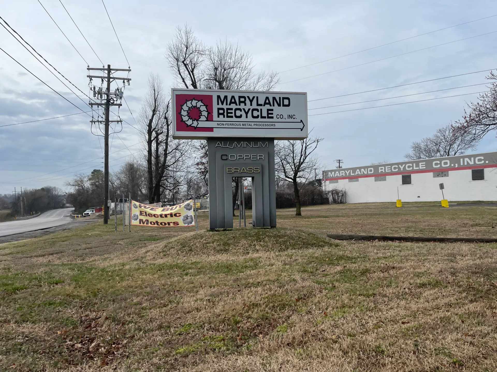 A sign for Maryland Recycle Co. stands on a grassy lot near a building marked Maryland Bicycle Co., Inc. under a sky.
