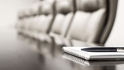 Notebook and pen on a conference table with blurred office chairs in the background