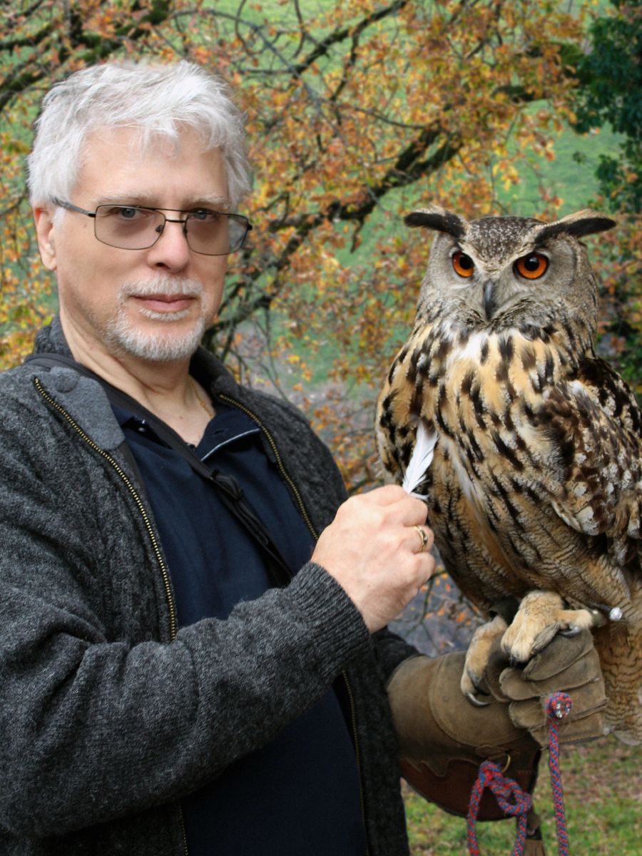 Constantine Karbaliotis holding a large owl on a gloved hand in a wooded outdoor setting