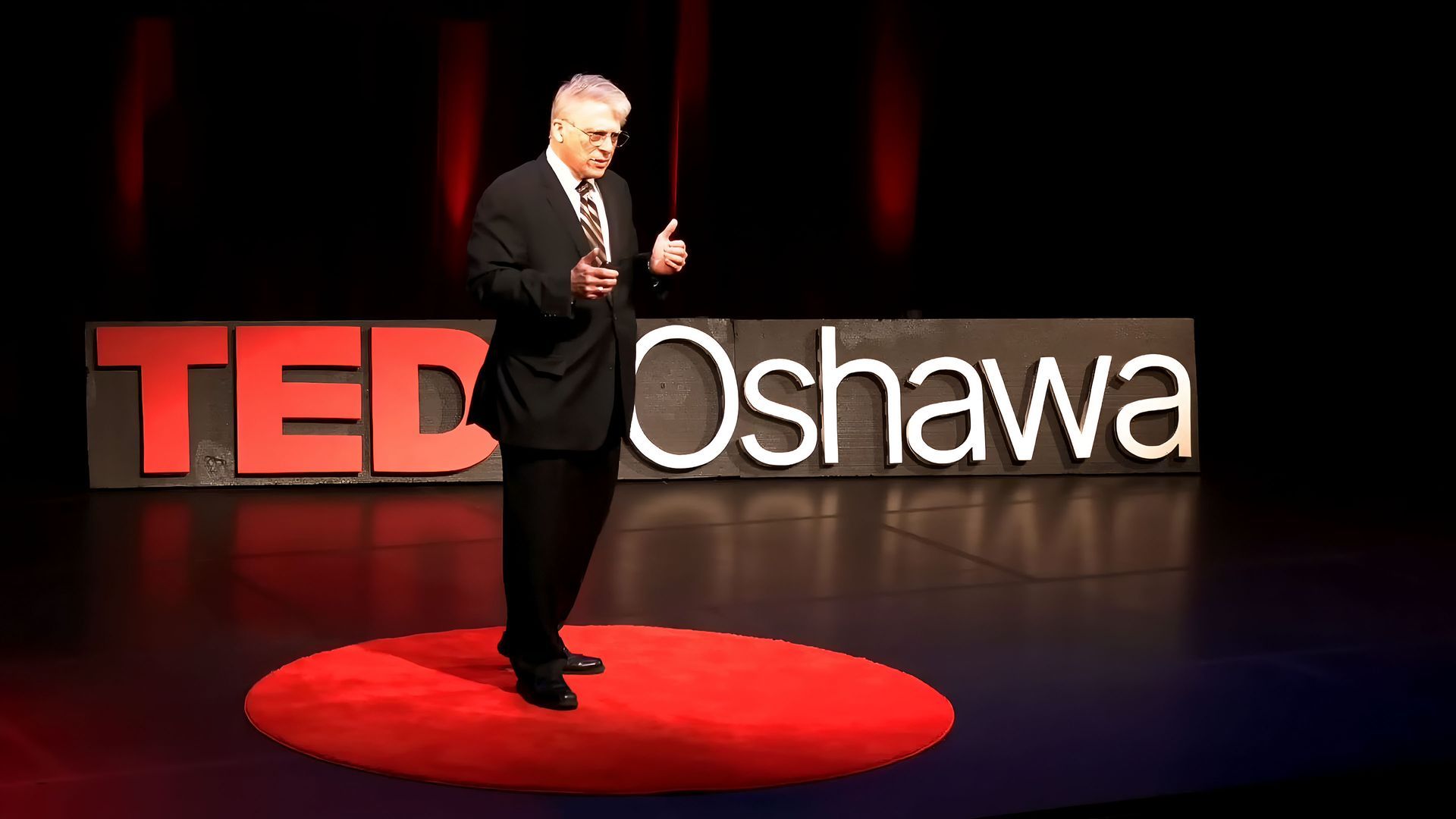 TEDxOshawa stage with a Constantine Karbaliotis on a red circular platform beside the illuminated TEDxOshawa sign