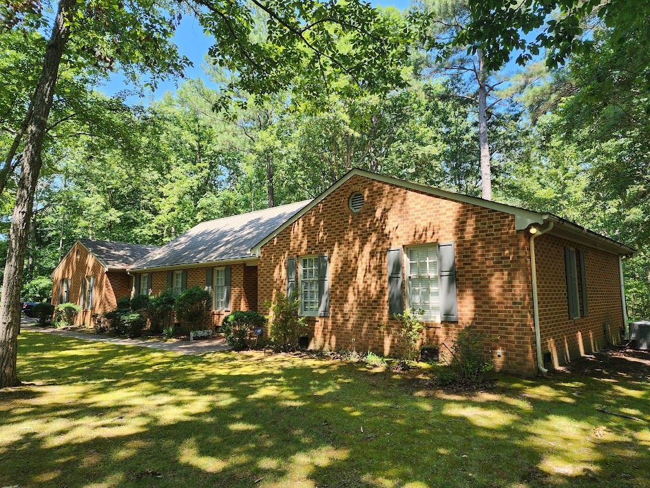 A large brick house is surrounded by trees on a sunny day.