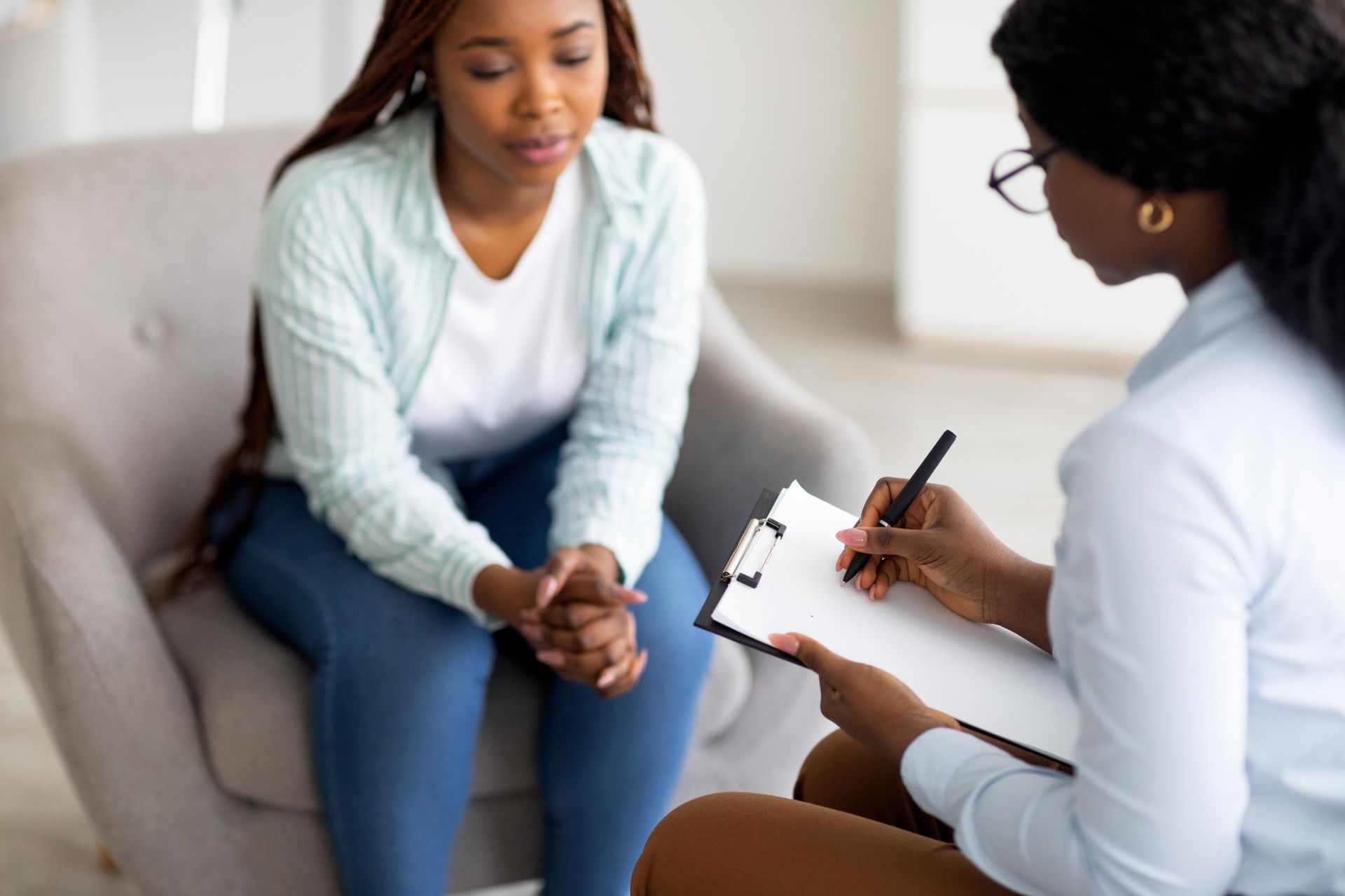 Two people in a counseling session, one taking notes on a clipboard.