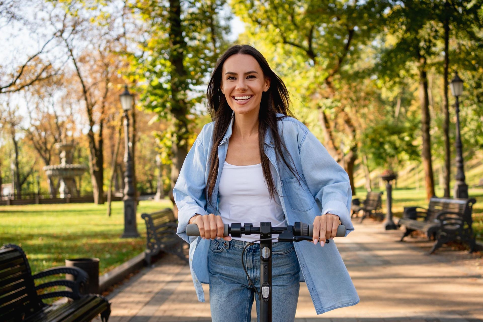 Smiling woman riding a bicycle on a tree-lined park path on a sunny day