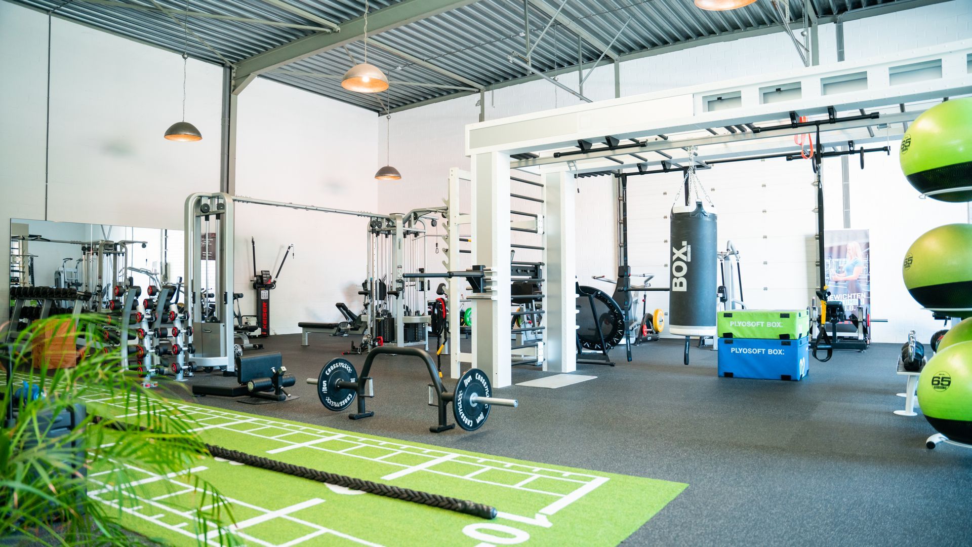 Een sportschool vol met fitnessapparatuur en een groene mat.