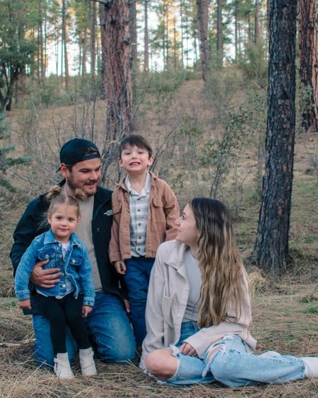 Family sitting together outdoors in a wooded area, smiling and relaxed.