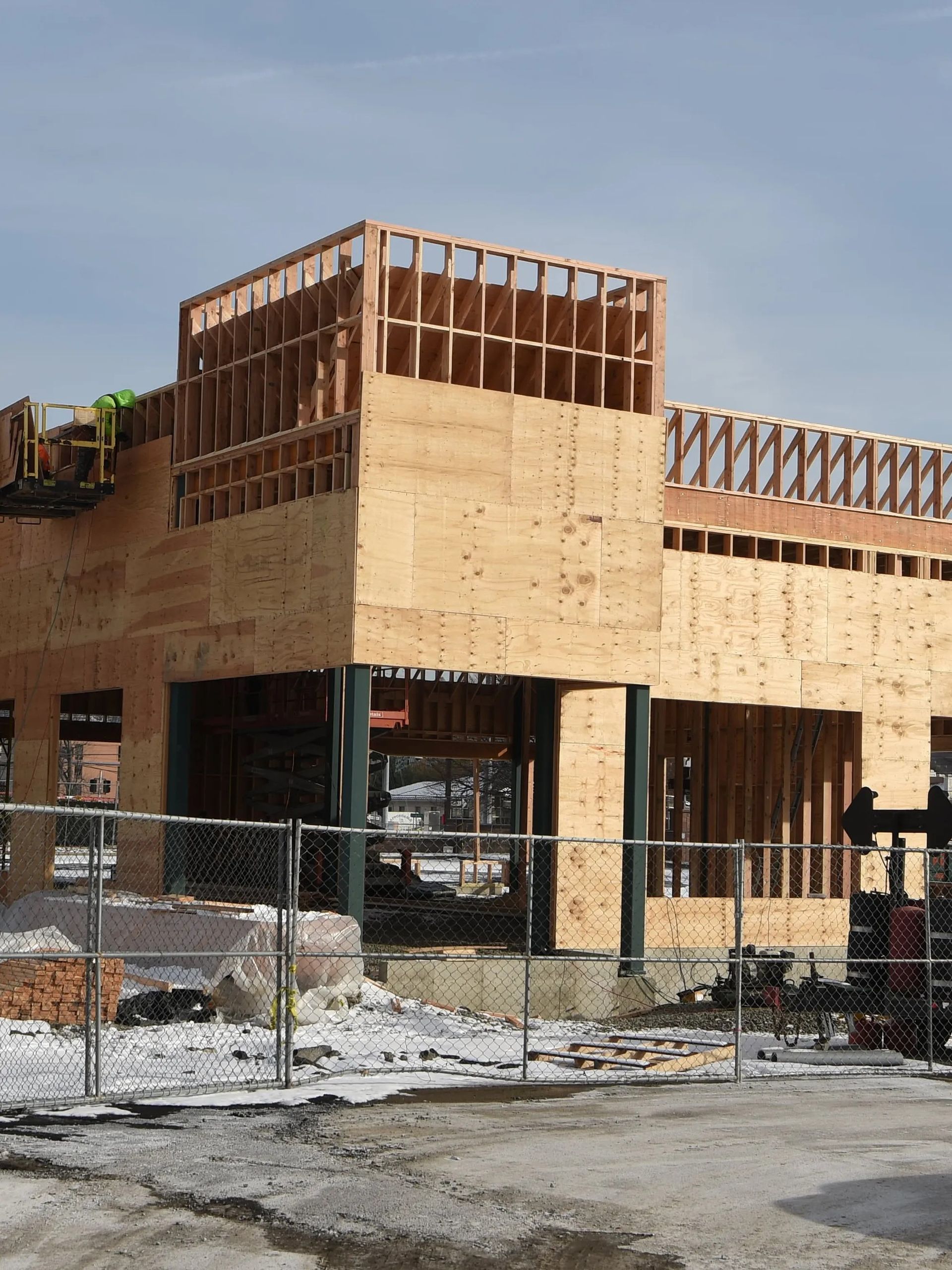 Partially built two-story wooden building with exposed framing behind a chain-link fence on a construction site