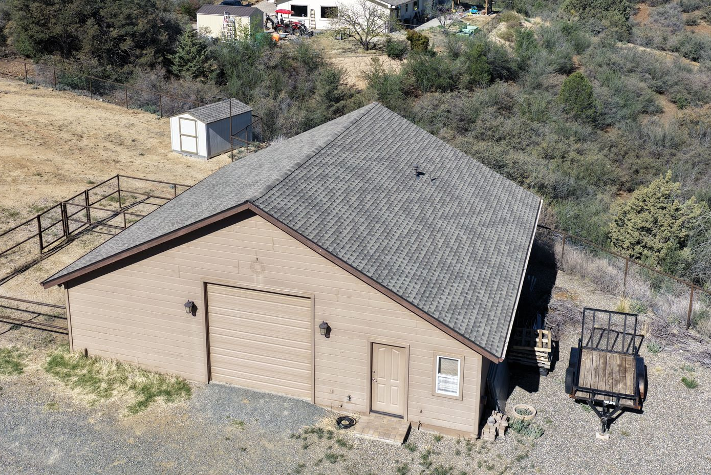 Aerial view of a tan utility building with a gray shingled roof on a gravel hillside.