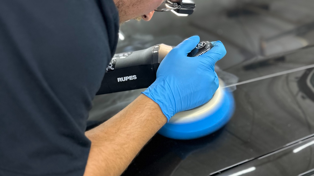 A man wearing blue gloves is polishing a car.