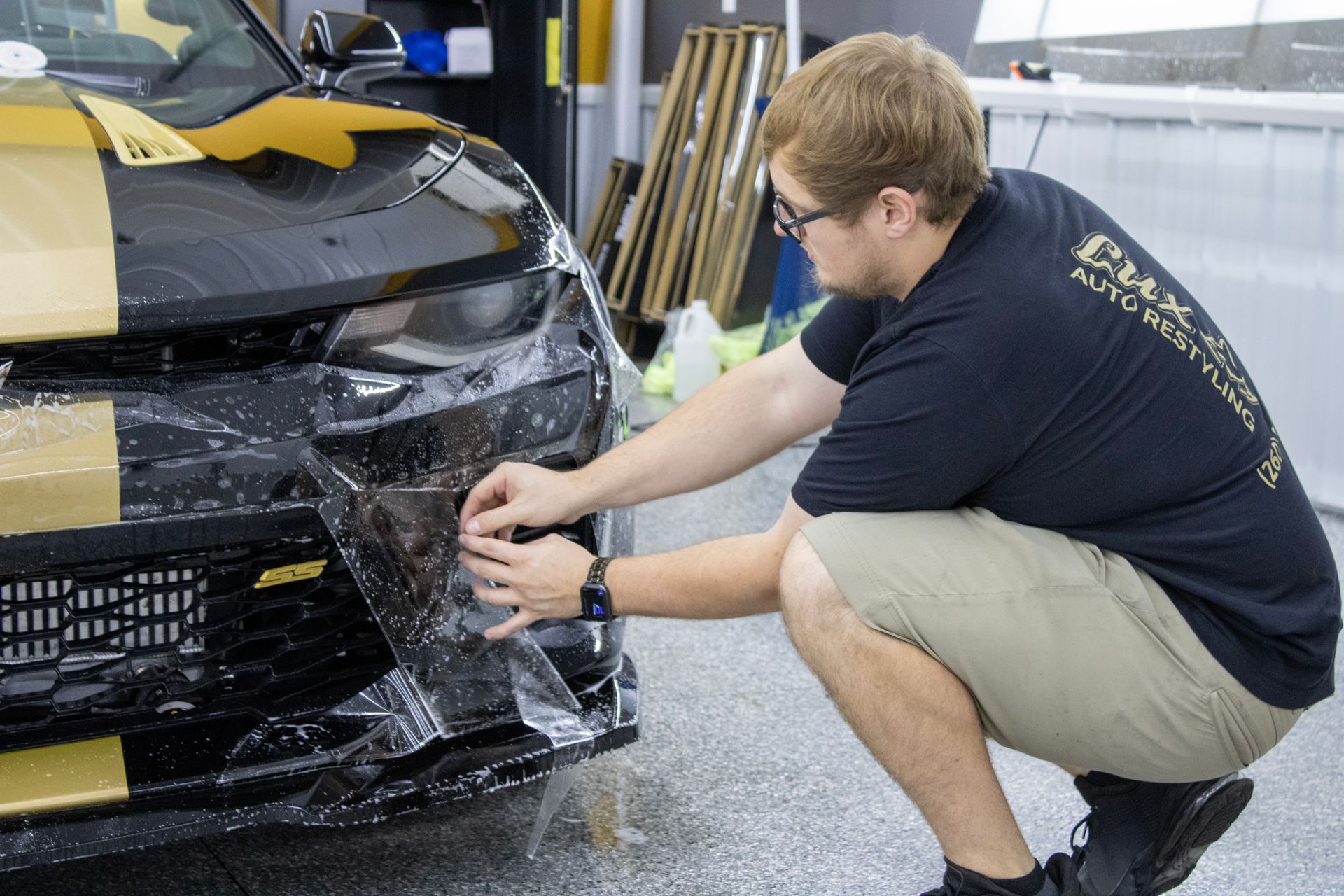 A man is wrapping the front of a car with plastic wrap.