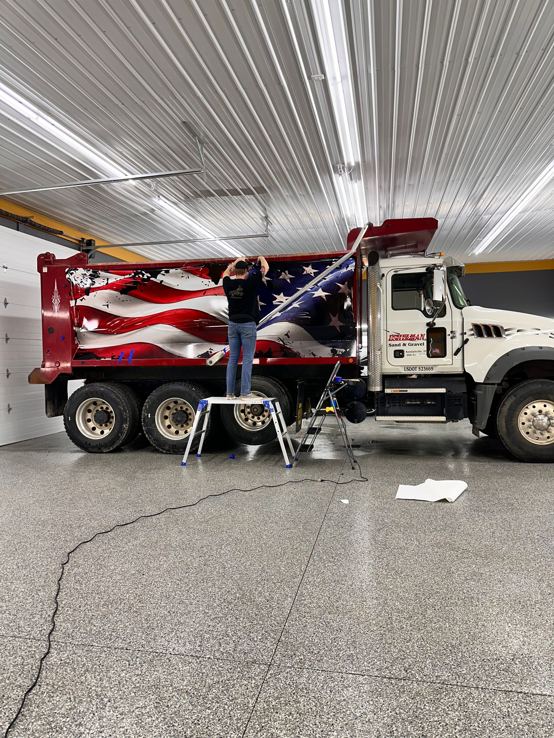 A man is wrapping an american flag on the side of a dump truck.