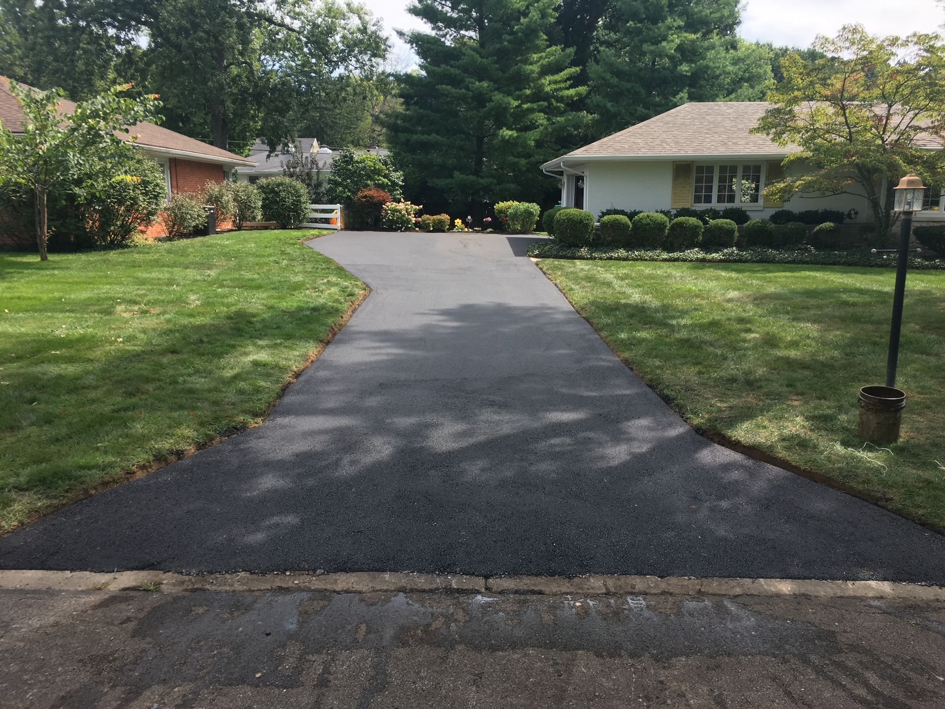 Freshly paved driveway leading to a suburban house with green lawns and trees on both sides