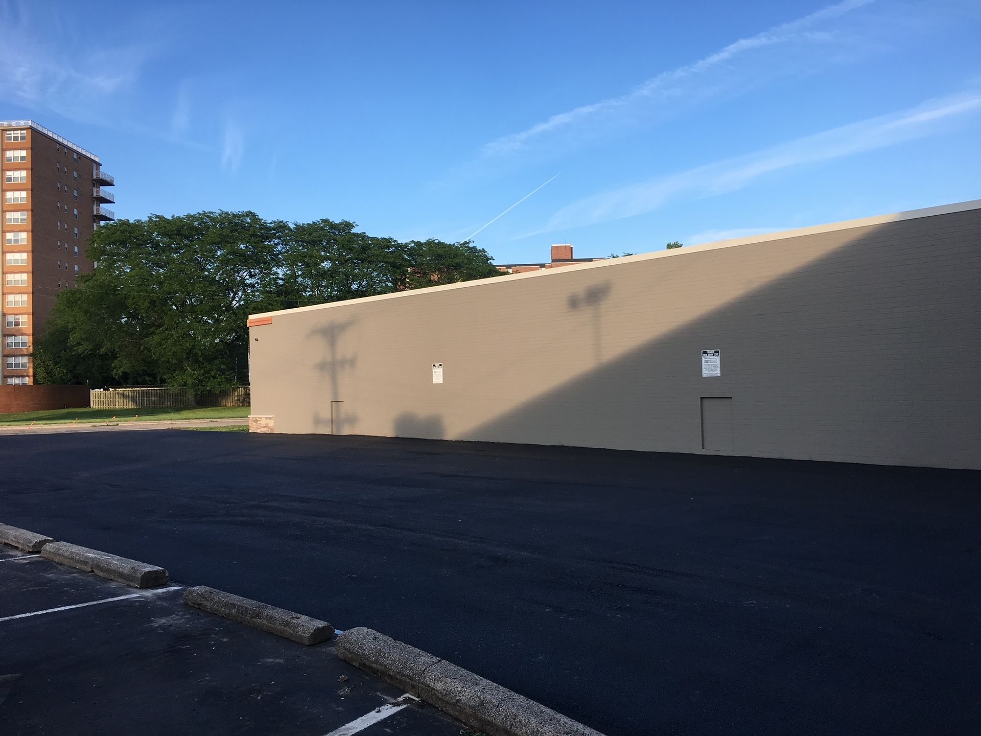 Empty parking lot beside a beige building and a brick apartment tower under a blue sky
