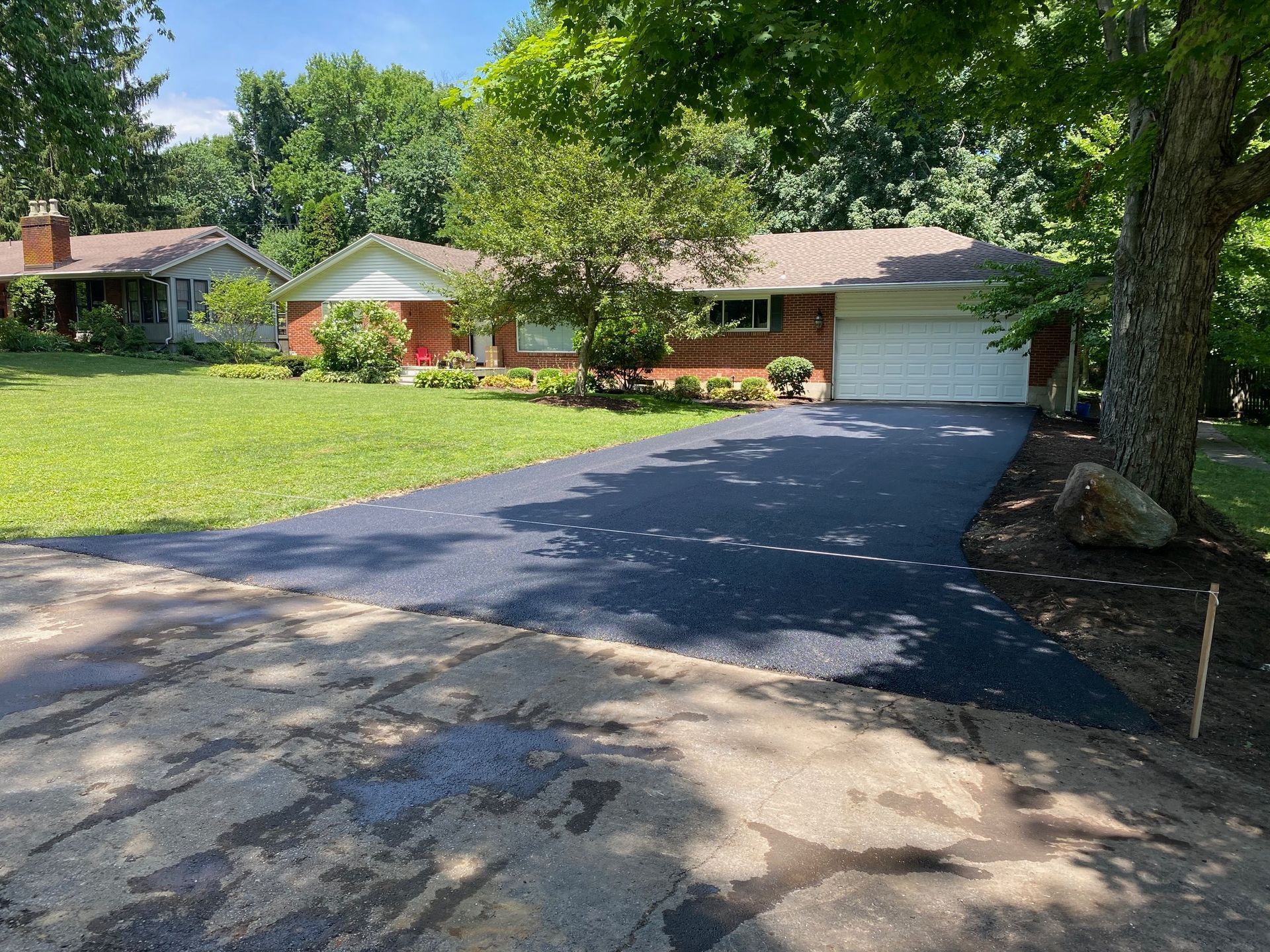 Suburban house with a paved driveway, green lawn, and large tree in the foreground