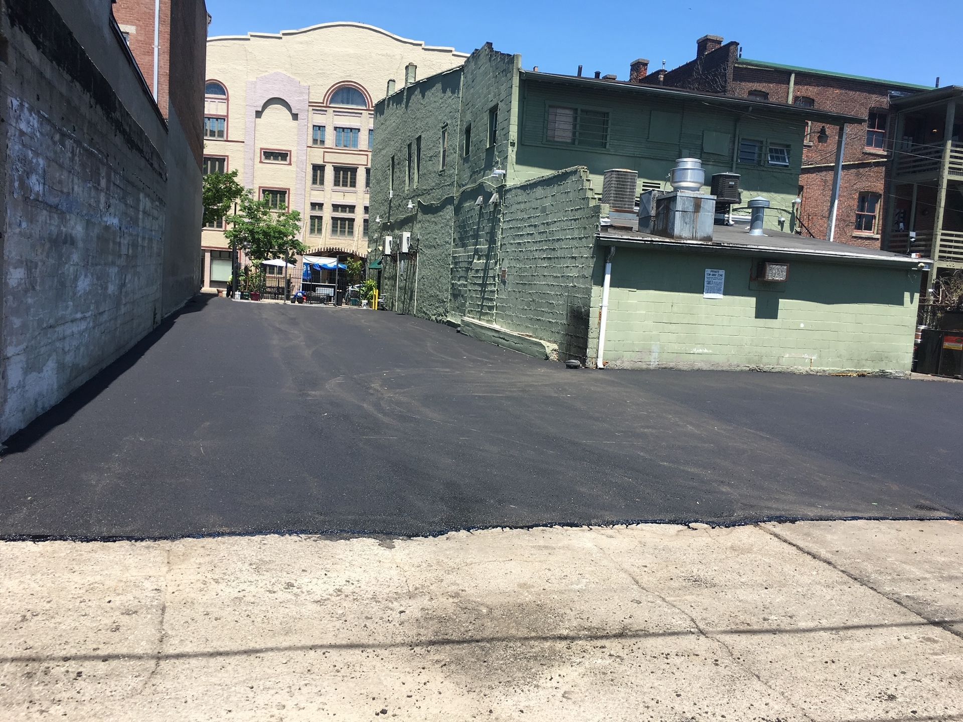 Empty paved alley between old brick buildings, with a light-colored building at the end.