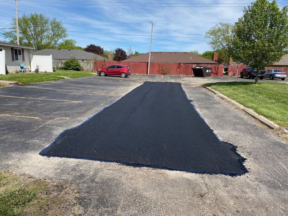 Fresh black asphalt laid over a driveway in a residential parking lot, with houses and cars in the background