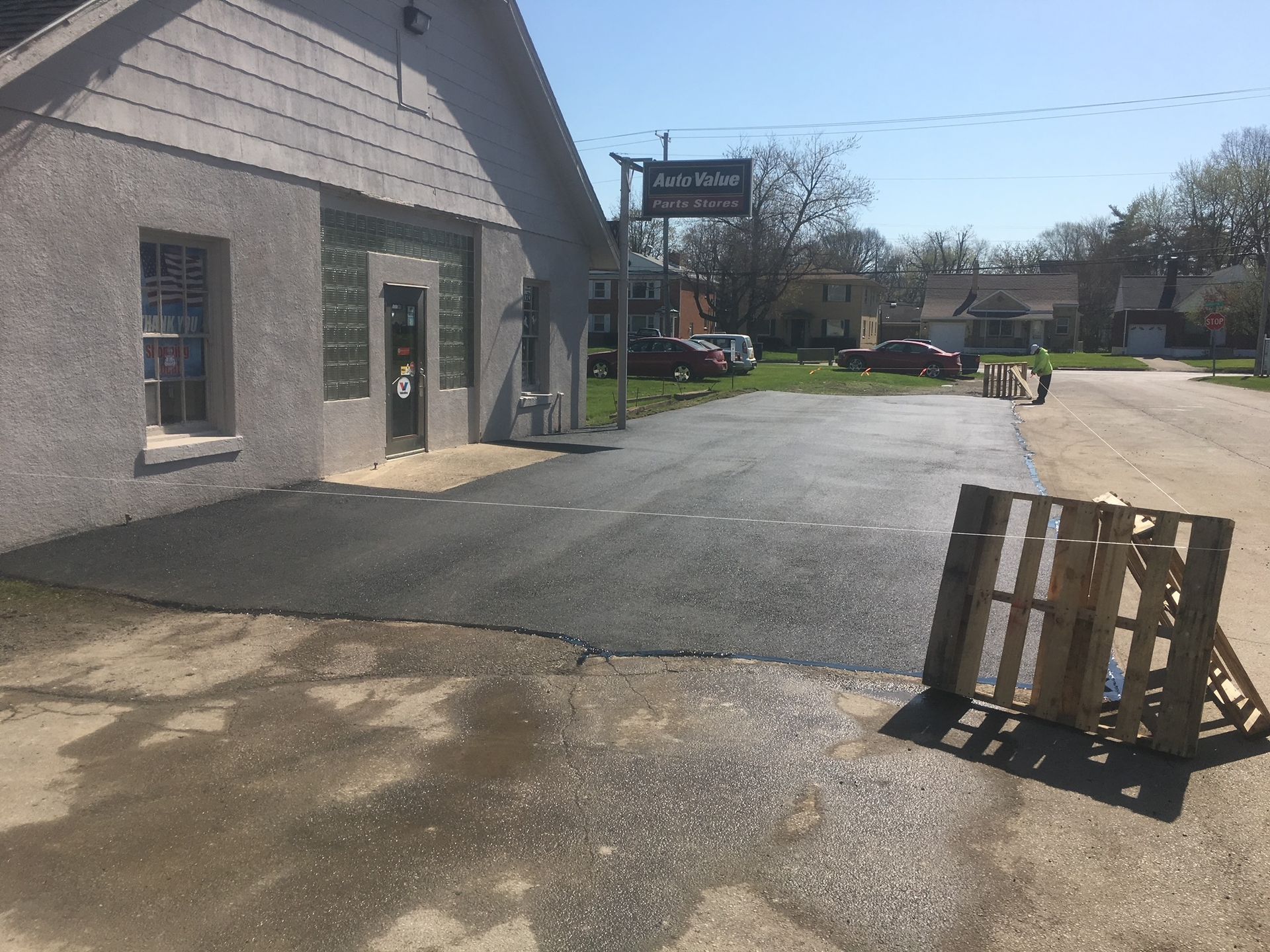 Empty parking lot beside a gray building, with a wooden pallet leaning on the asphalt.