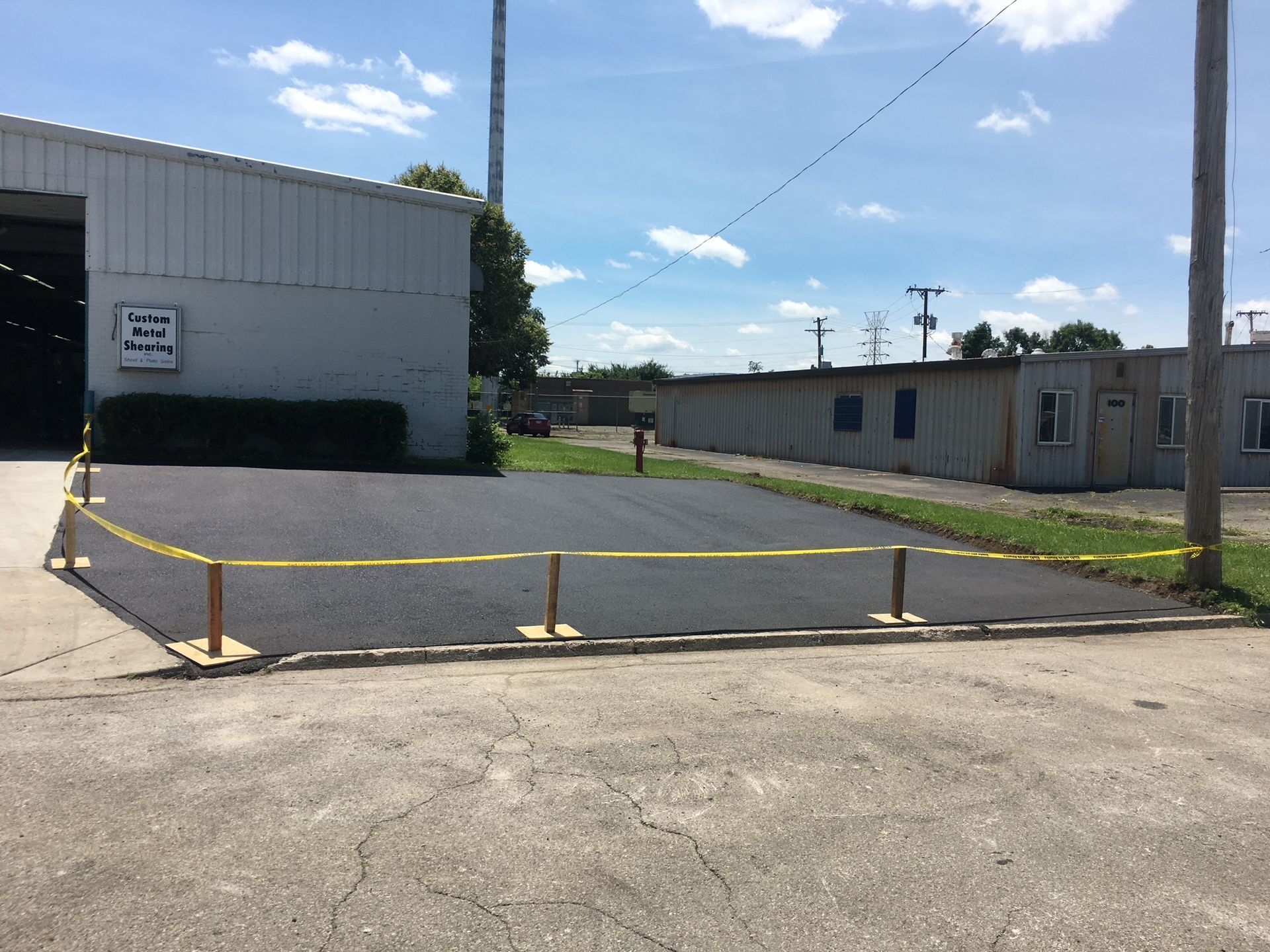 Empty paved lot with yellow barrier tape beside industrial buildings under a blue sky