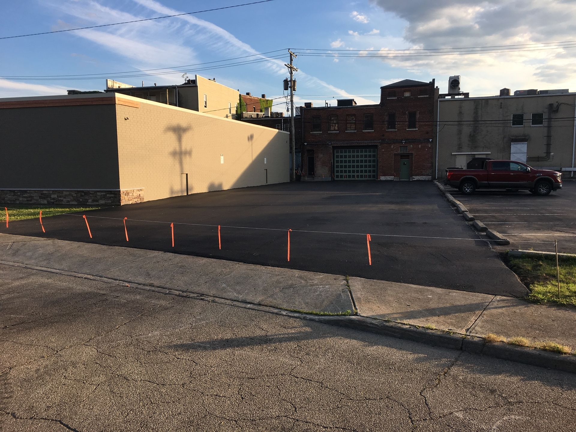 Empty parking lot beside brick buildings at sunset, with orange cones lining the edge of the pavement.