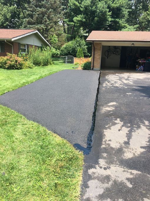 Freshly paved black driveway beside a garage and green lawn on a sunny day