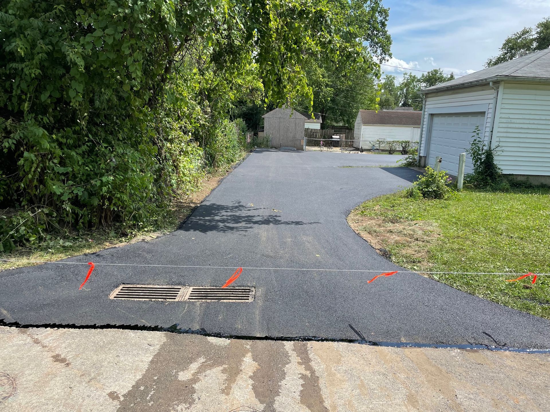 Fresh blacktop driveway with orange markers, trees on the left, and a white garage on the right.
