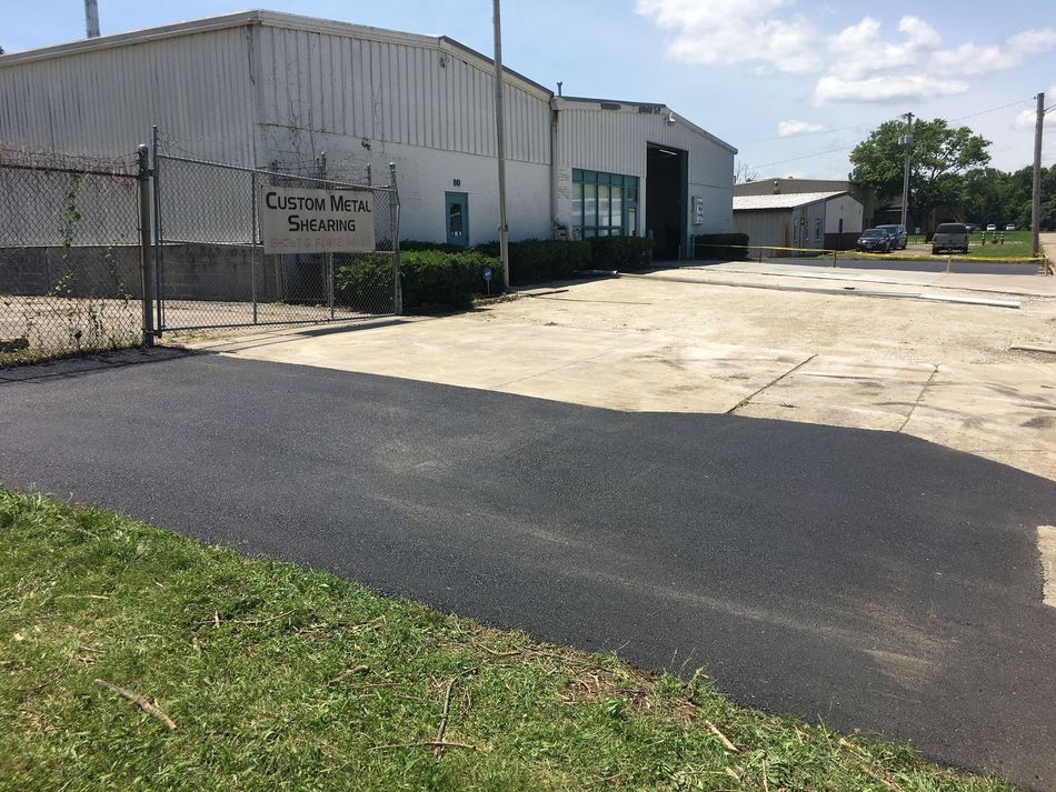 Warehouse buildings with a black driveway and grassy foreground on a sunny day