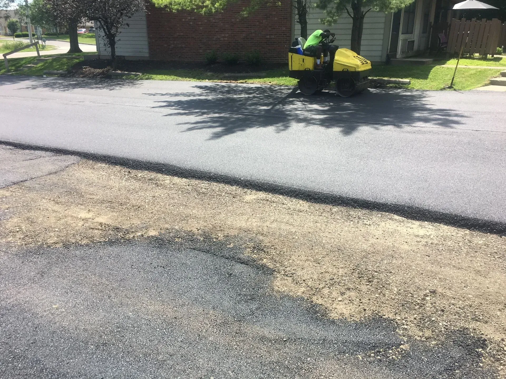 Worker with yellow equipment repairing pavement on a suburban street.