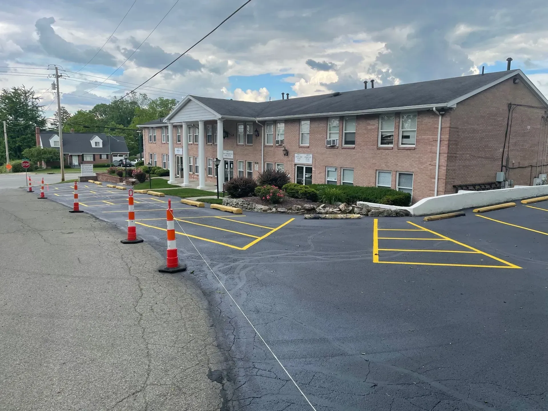 Parking lot beside brick building with orange cones and yellow painted lines after resurfacing