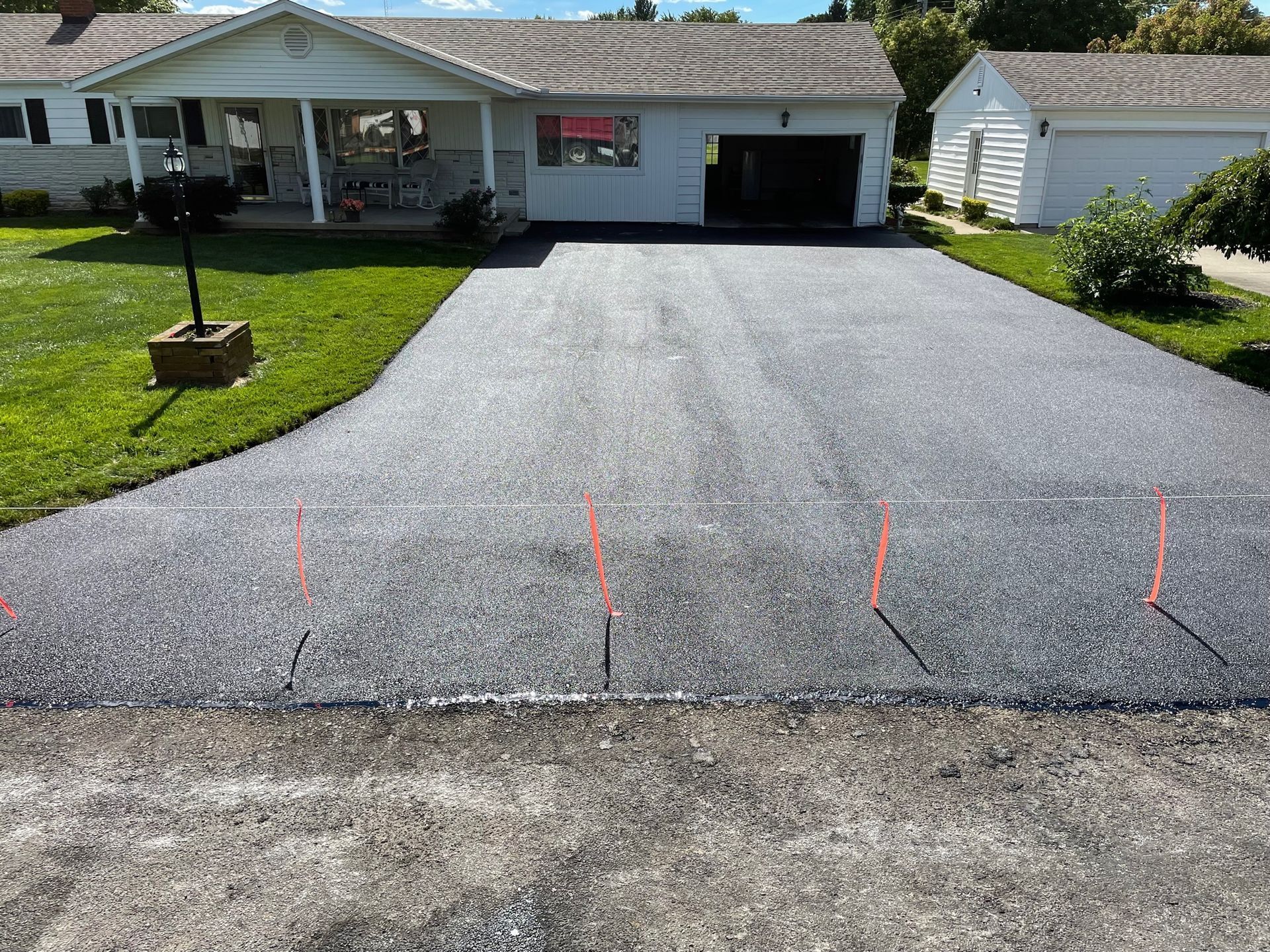 Freshly paved gray driveway leading to a single-story house with a garage and lawn