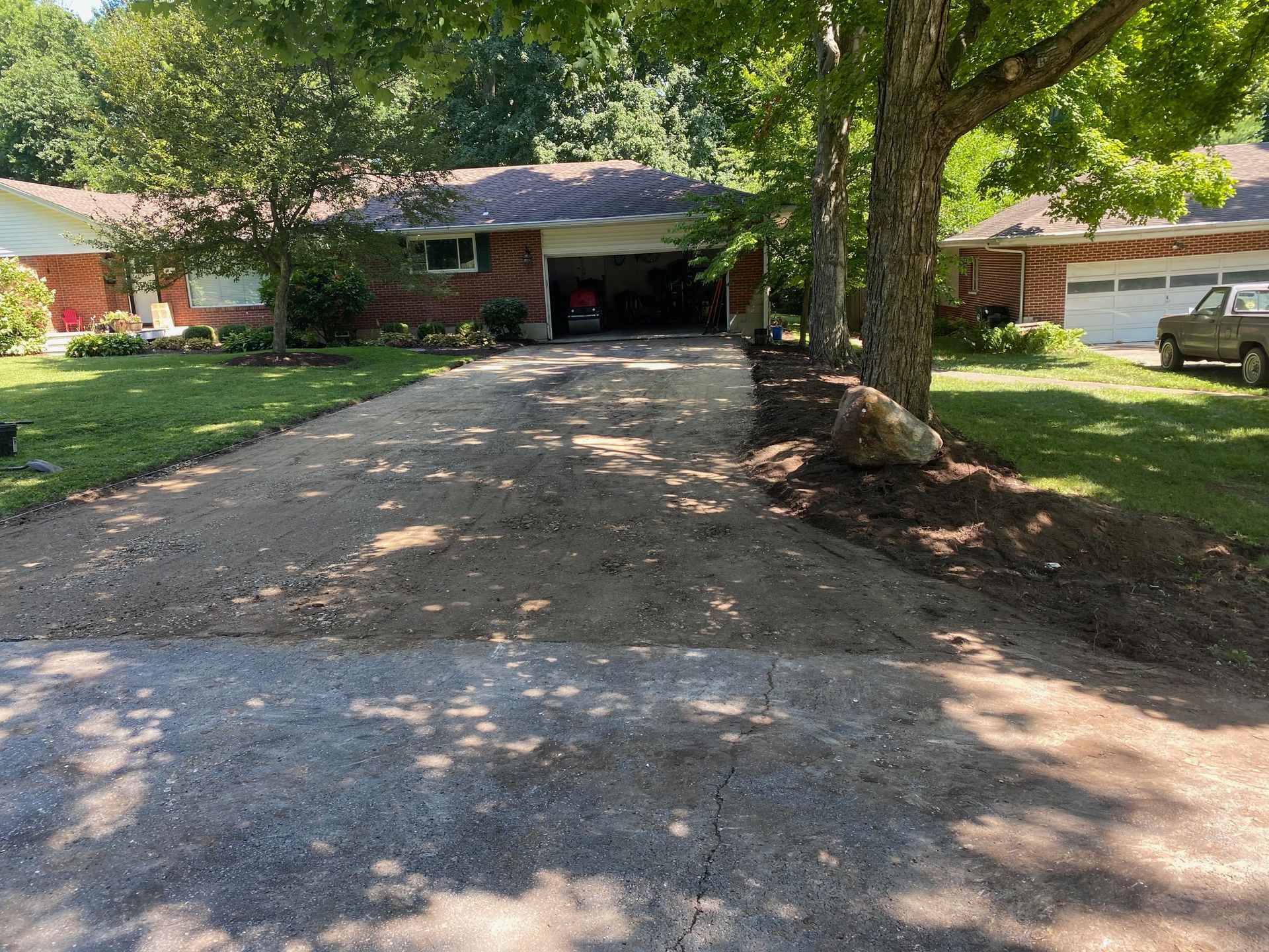 Gravel driveway leading to a house with trees and a parked truck on the right