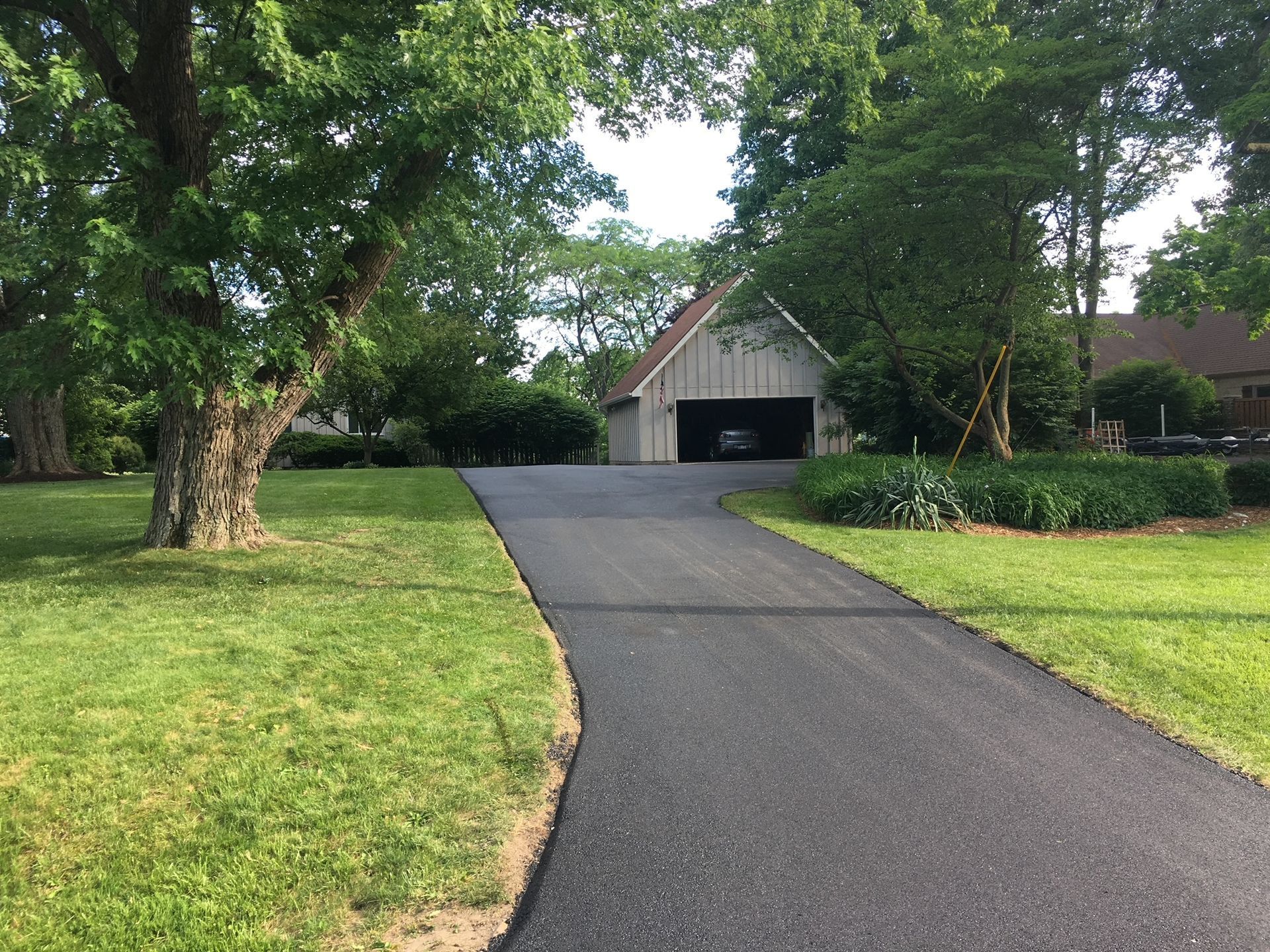 Long driveway leading to a detached garage, bordered by green lawns and trees.