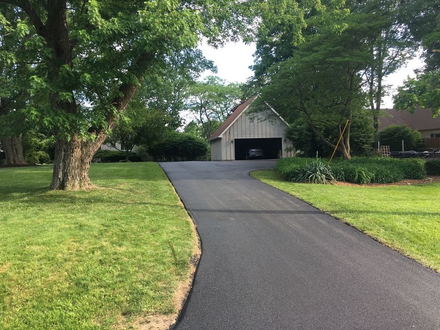 Suburban driveway leading to two houses with green lawns and trees on a sunny day
