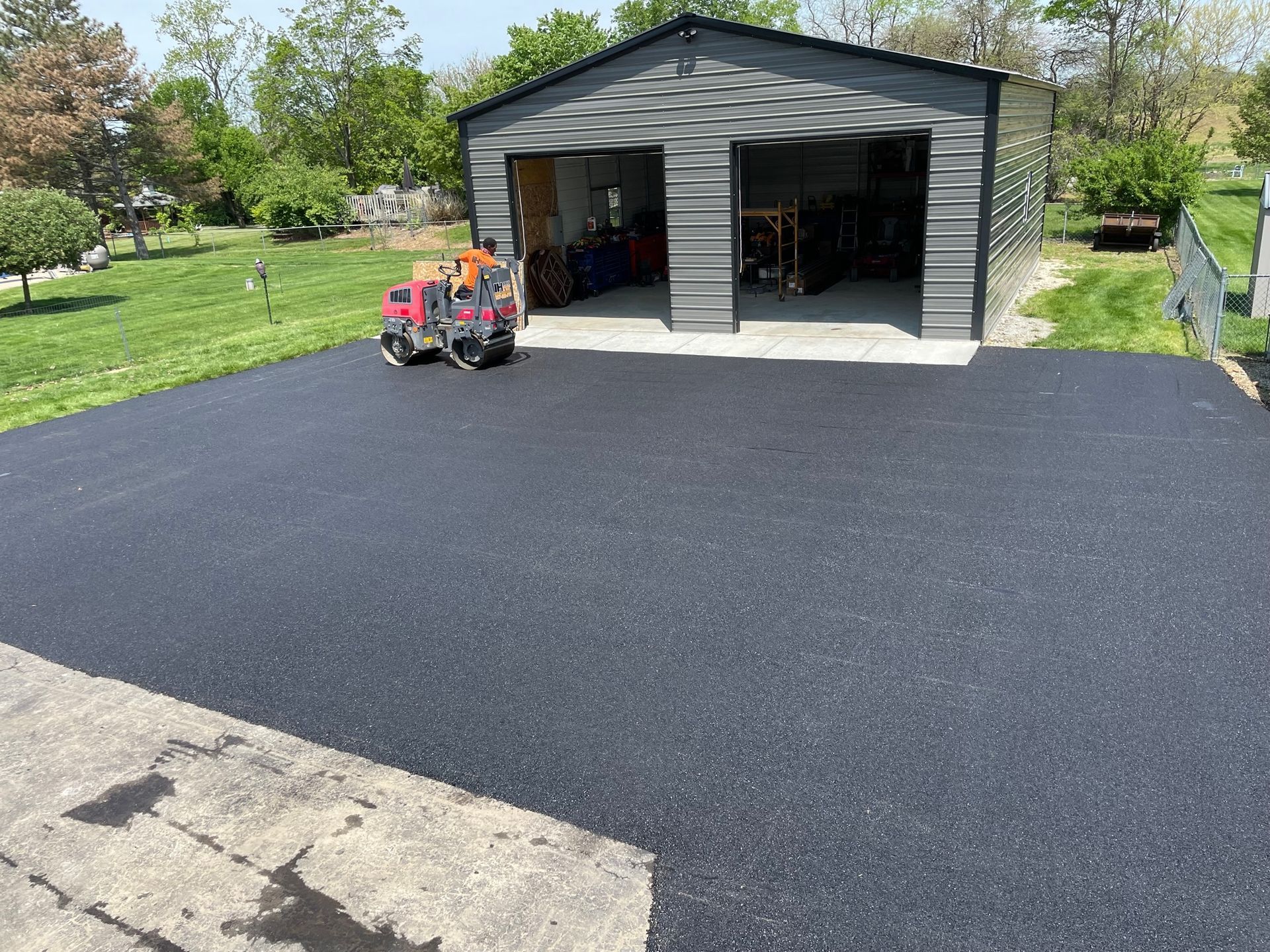 Freshly paved driveway leading to a gray garage with a red riding mower nearby