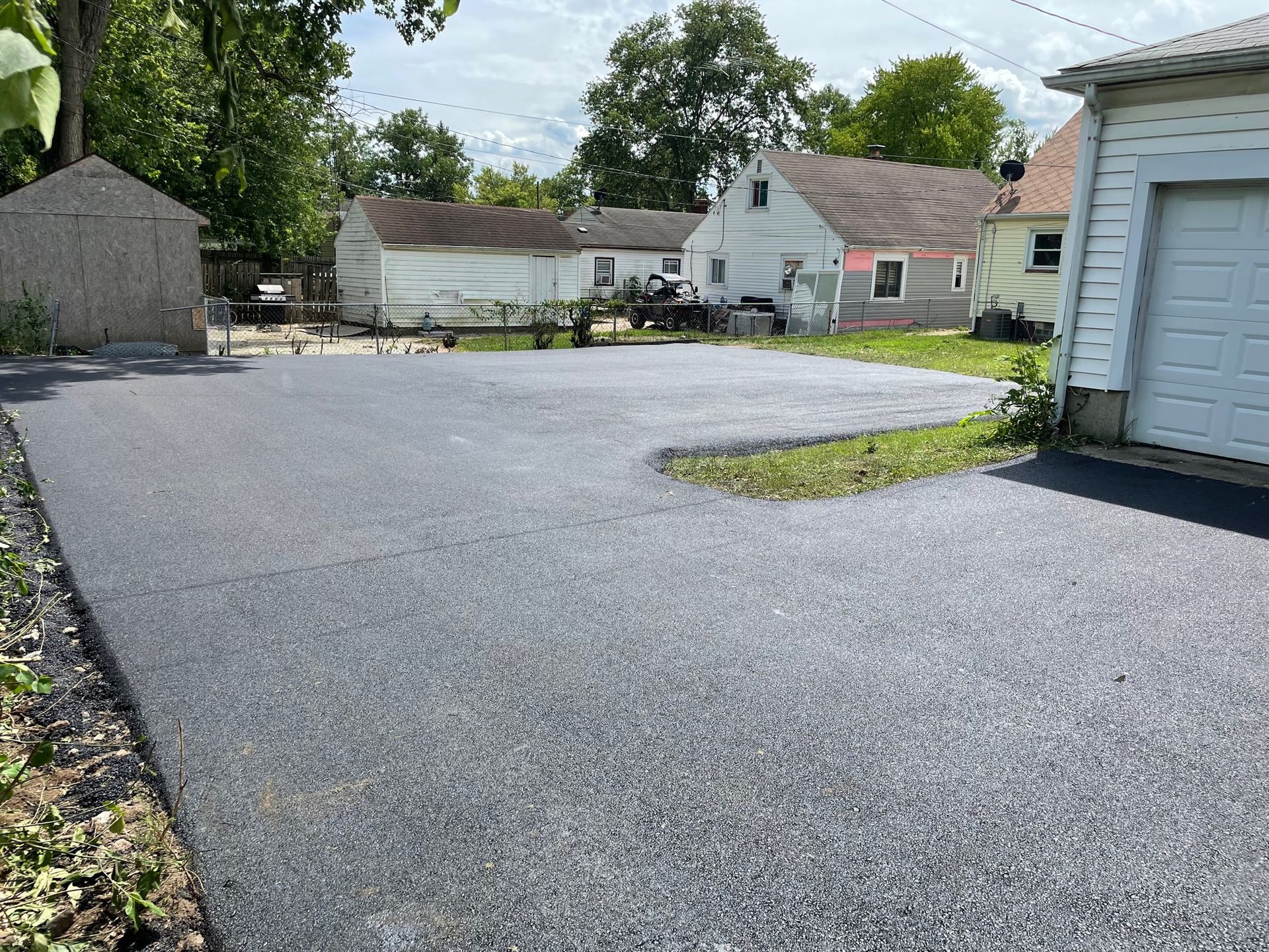 Quiet residential parking lot with gray pavement, small houses, and trees on a sunny day