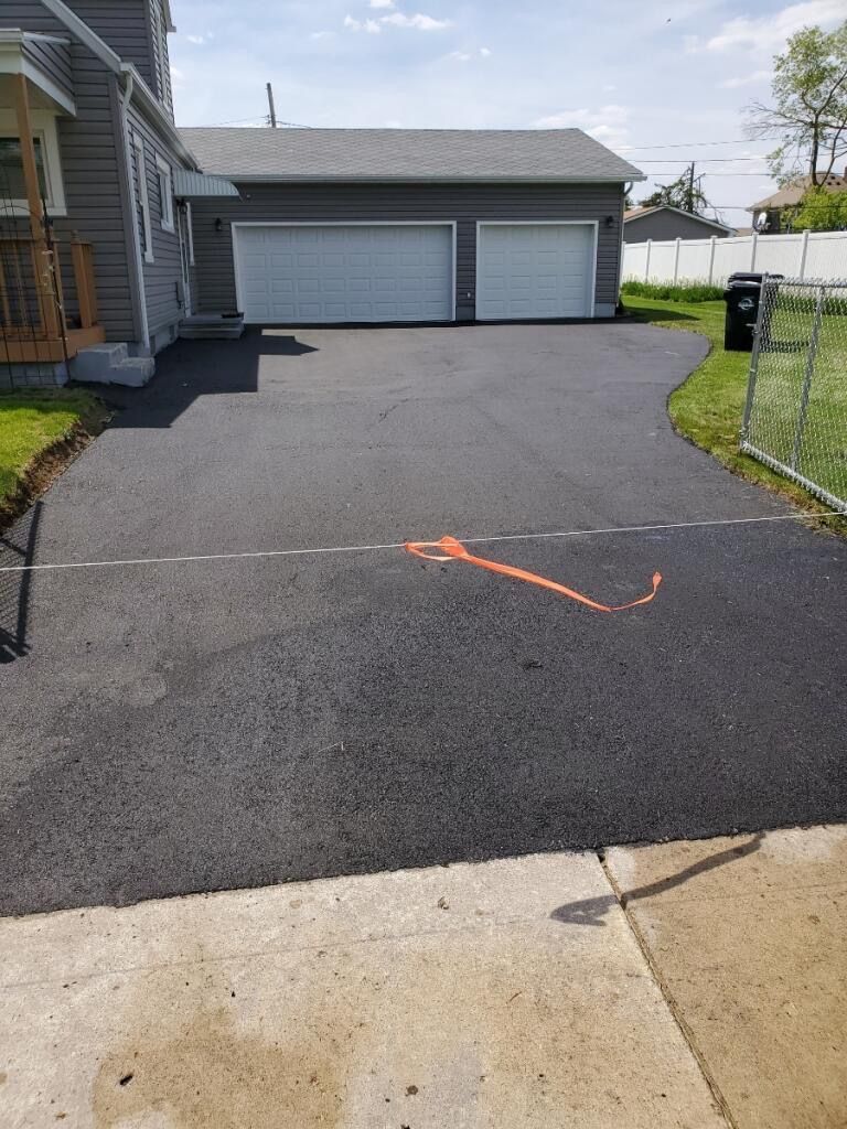 Driveway to a garage with fresh black asphalt and an orange spray-painted mark near the center.