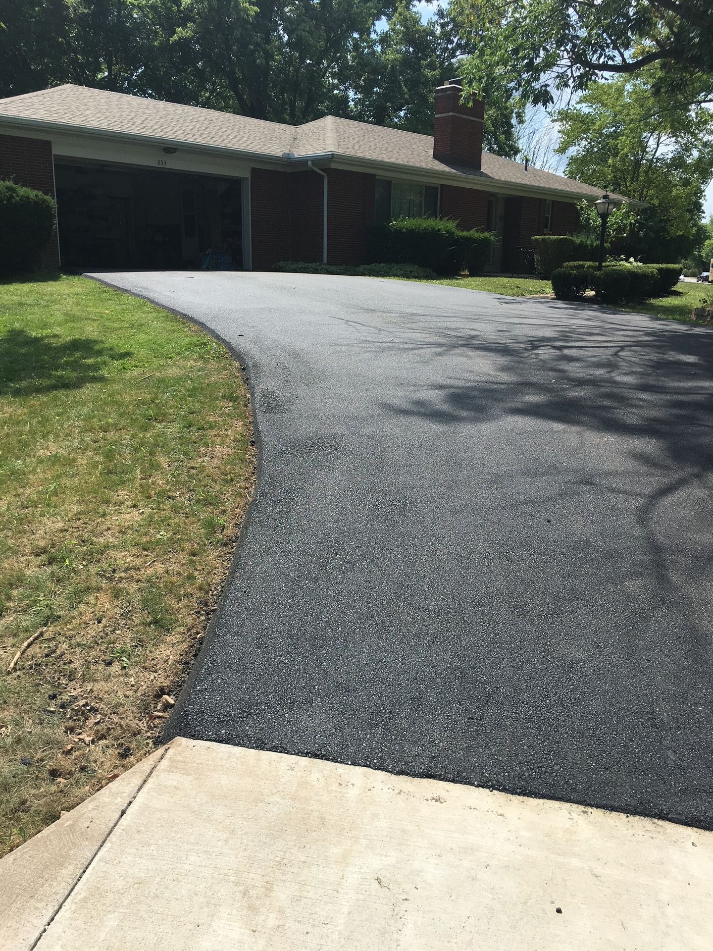 Curved driveway leading to a single-story house with a dark garage and green lawn under bright sunlight
