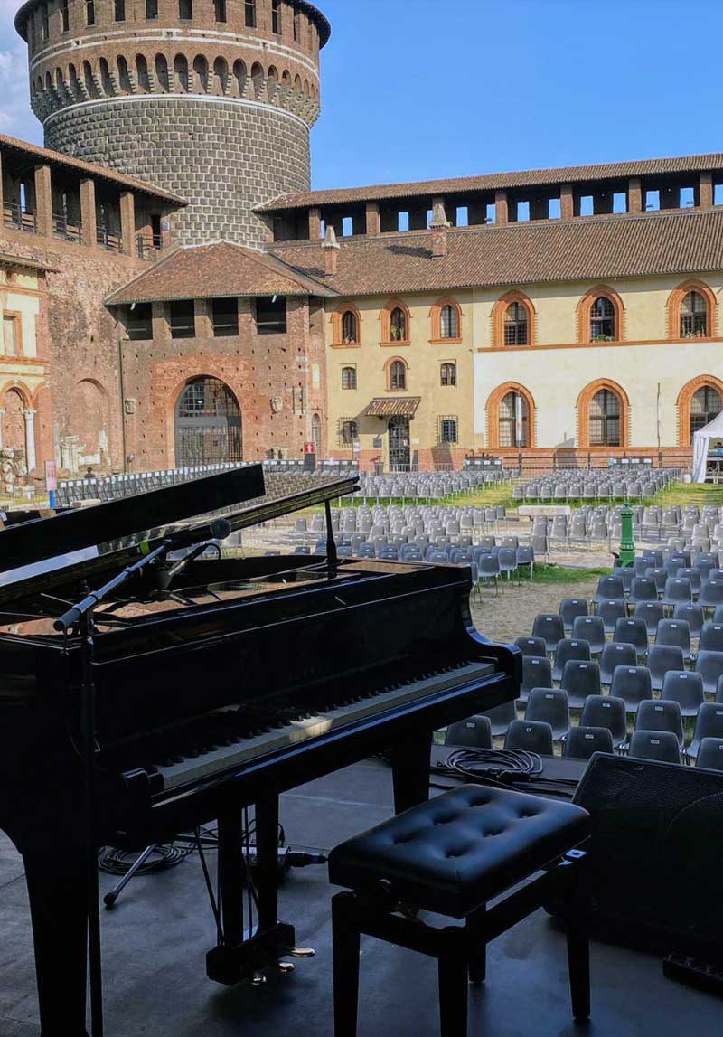 Un pianoforte è posizionato di fronte a un grande edificio con una torre sullo sfondo