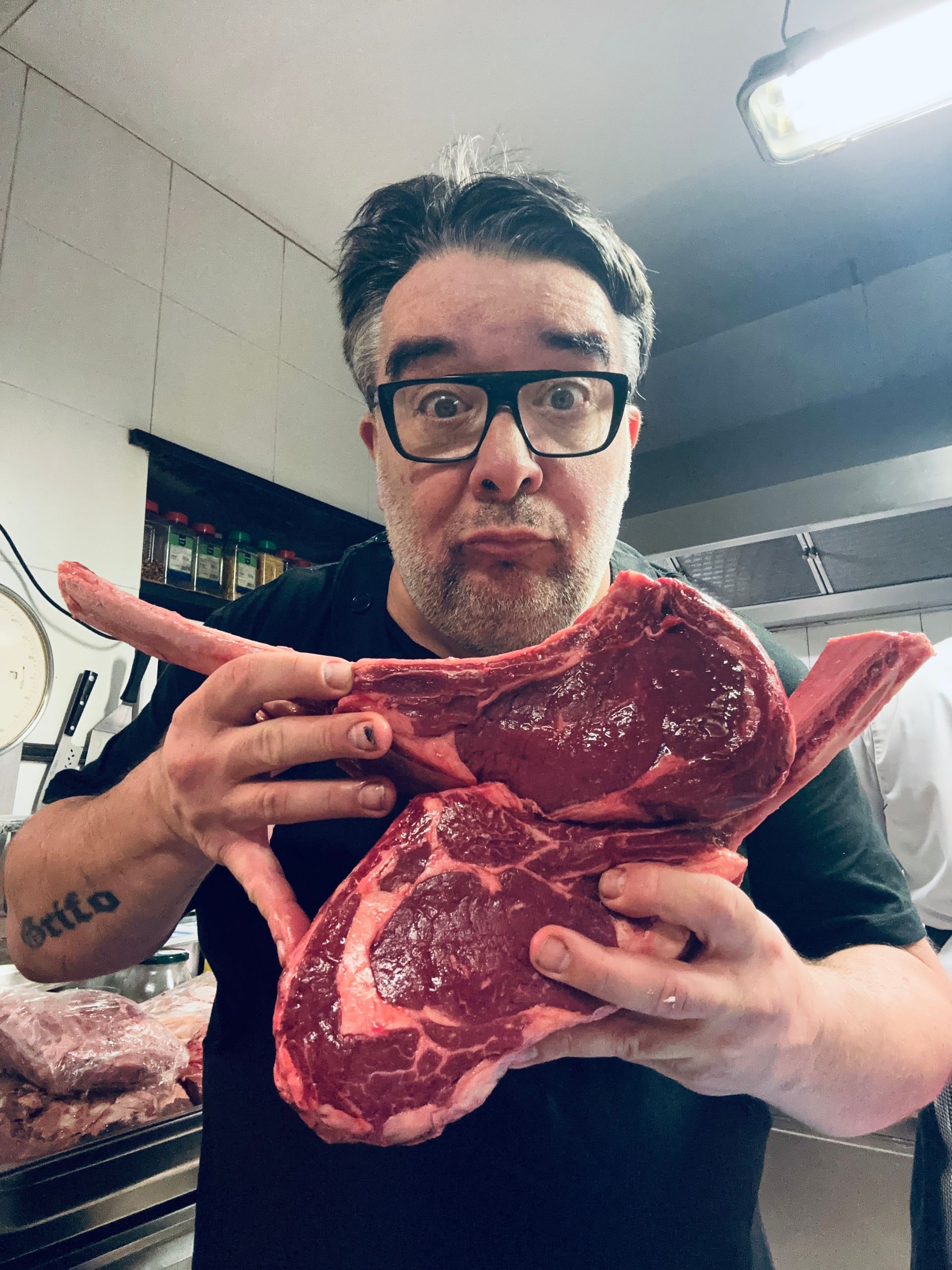 Un uomo tiene in mano due grosse bistecche crude in cucina e fa una smorfia.