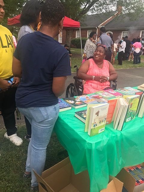 A woman in a wheelchair sits at a table full of books at a LCRC community event.